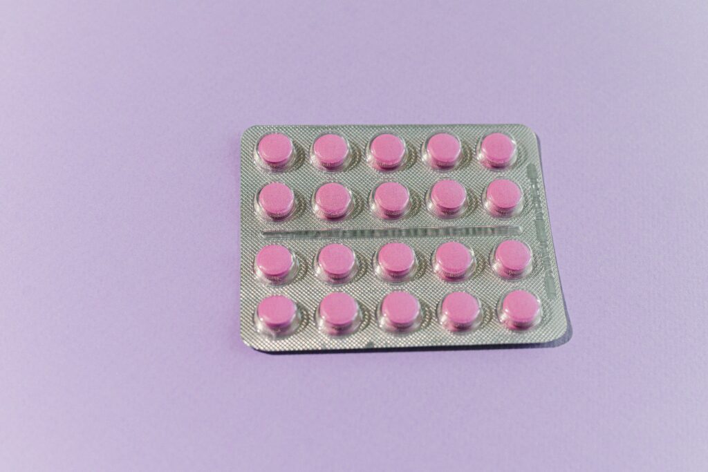 A neatly arranged blister pack containing pink tablets on a solid purple surface.